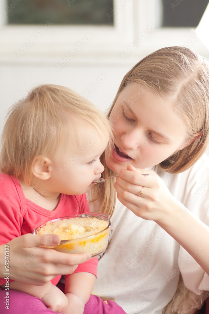 young adorable mother feeding his daughter with porridge young adorable mother feeding his daughter with porridge