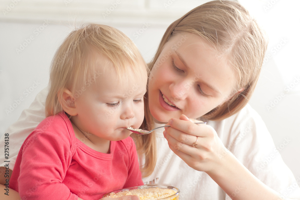 young adorable mother feeding his daughter with porridge young adorable mother feeding his daughter with porridge