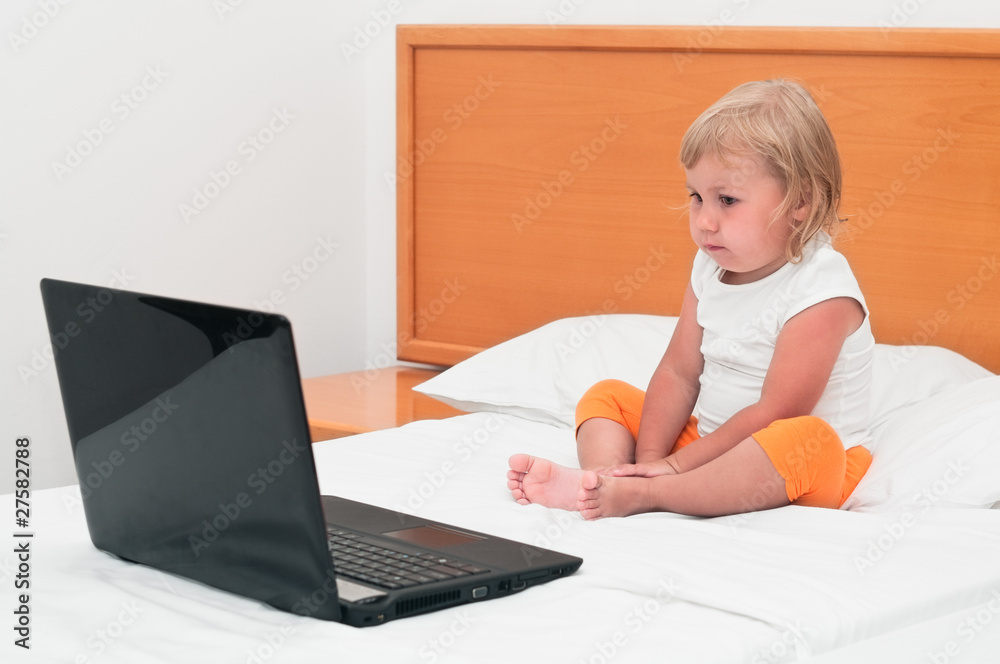 A small child is sitting with a laptop on the bed