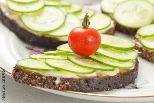 small red tomato on piece of rye bread with sliced cucumbers and