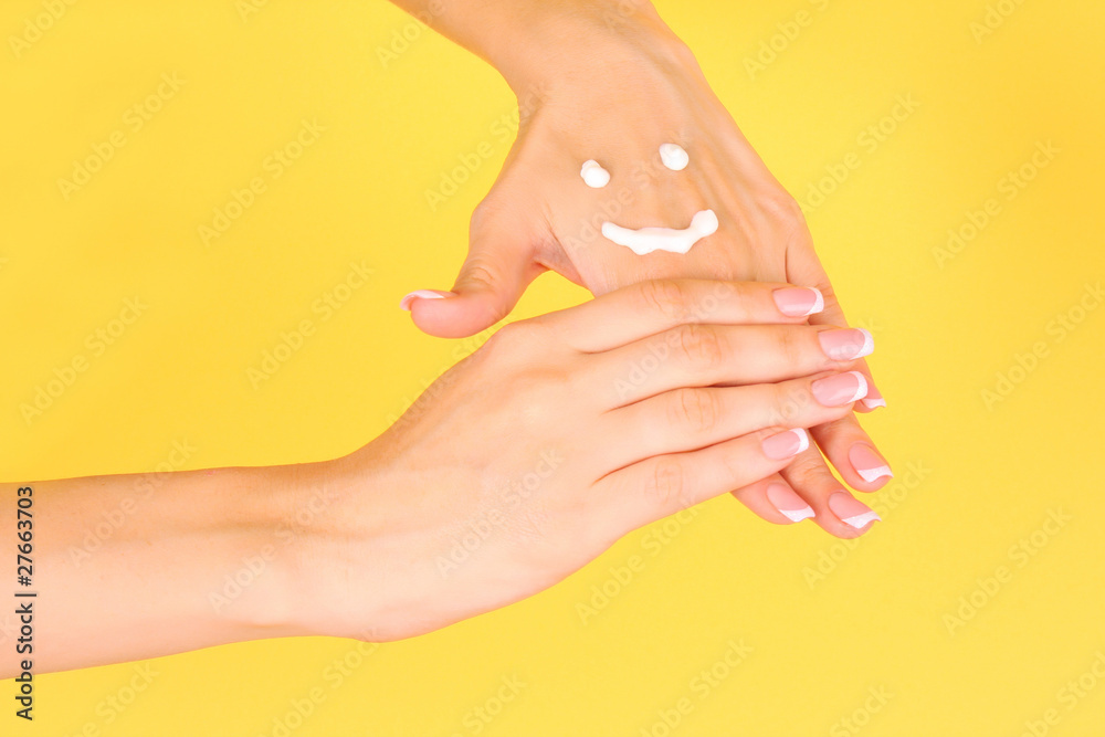 Closeup of beautiful female hands applying hand cream  on yellow