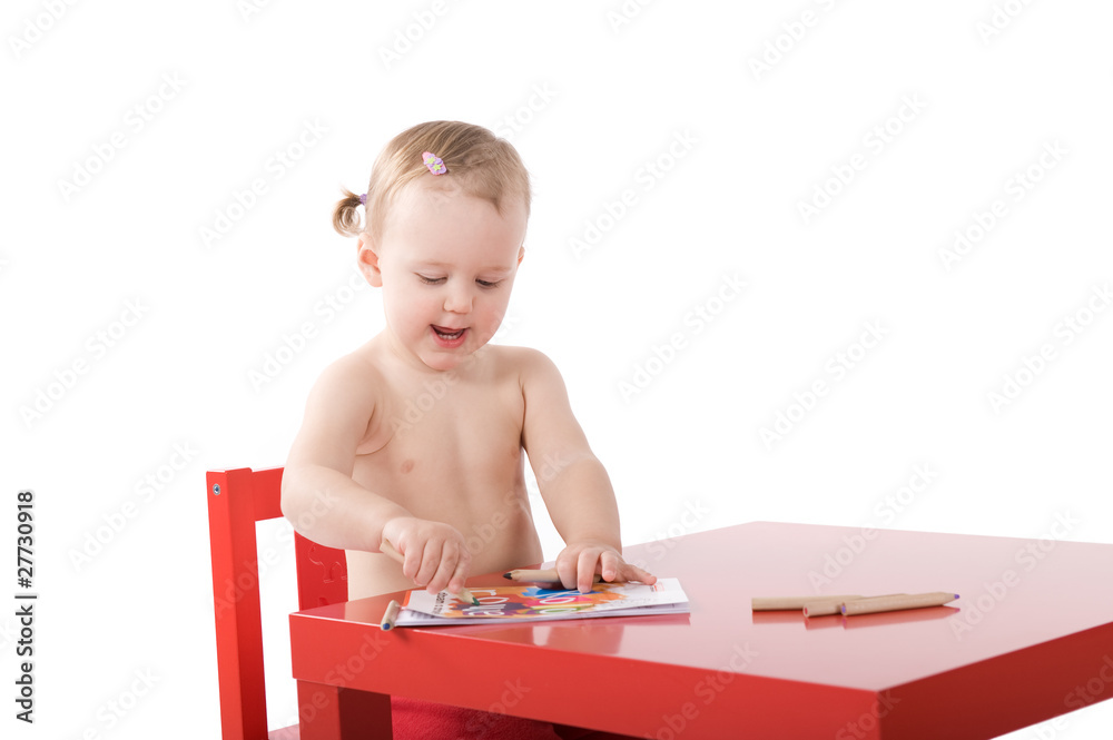 Little baby girl is sitting on the red chair and colouring