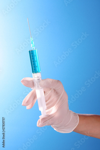 Syringe in doctors hand over blue background