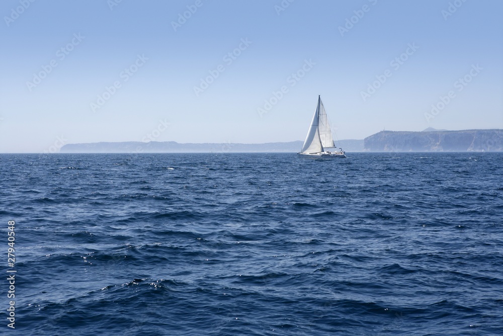 Blue sea with sailboat sailing the ocean surface