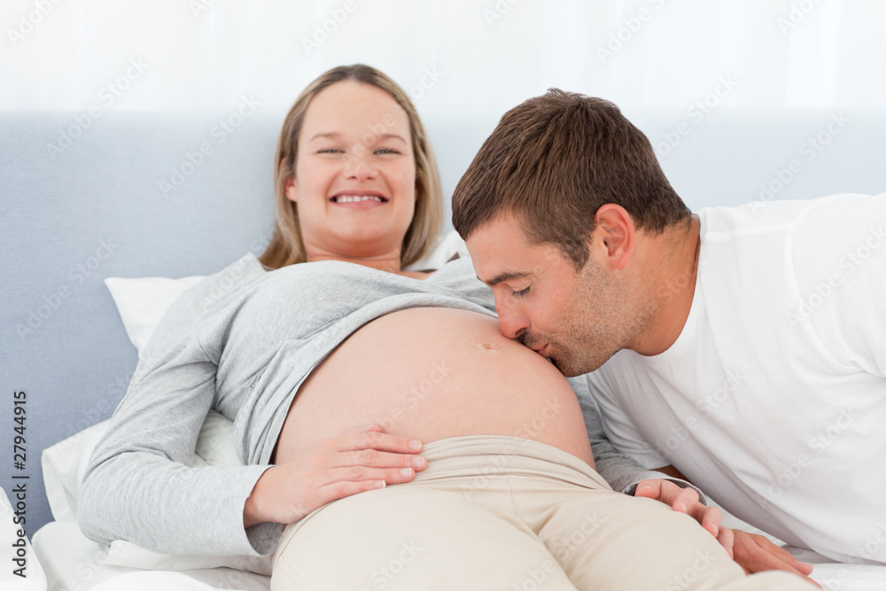 Happy man kissing the belly of his pregnant wife in the bed Happy man kissing the belly of his pregnant wife in the bed