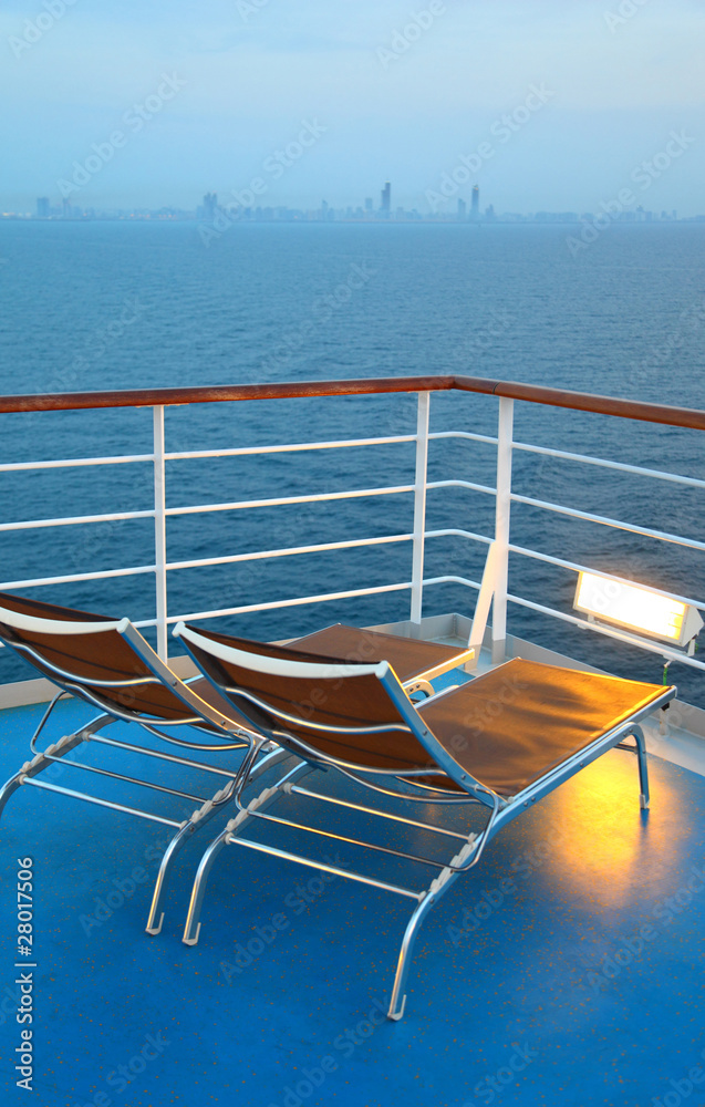 Two illuminated deck-chair on ship deck overlooking city Two illuminated deck-chair on ship deck overlooking city