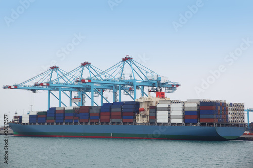 Big cargo boat docked to industrial port with several blue crane