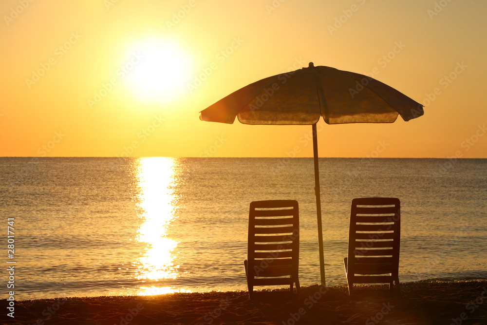 Two empty chairs stand on beach under opened umbrella with vi Two empty chairs stand on beach under opened umbrella with vi