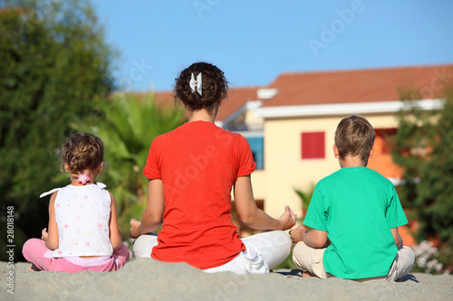 Mother with two children turned the backs, sit in pose of yoga