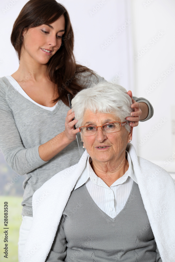 Young woman doing an haircut to old woman Young woman doing an haircut to old woman