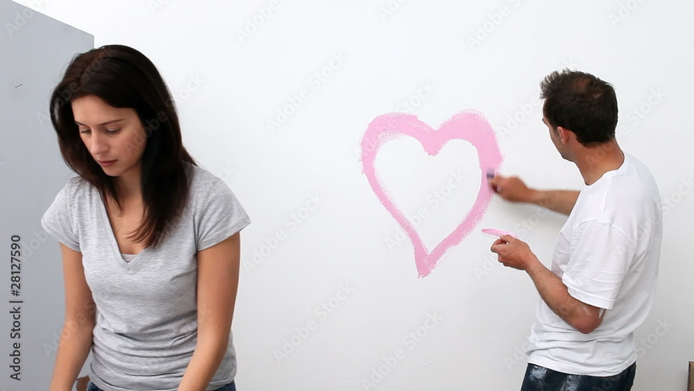 Man painting a heart while renovating a room with his wife Man painting a heart while renovating a room with his wife