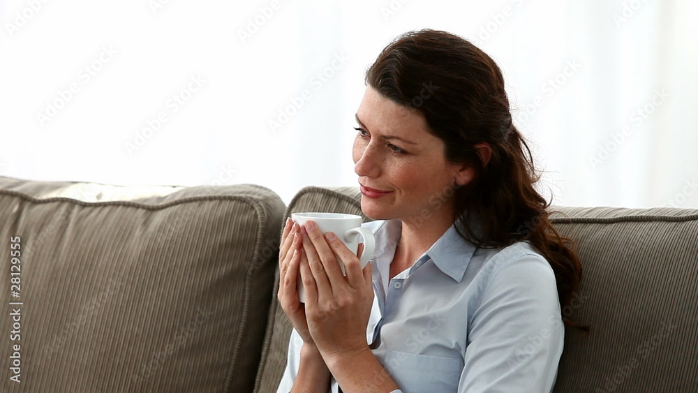 Pretty woman holding a cup of coffee sitting on the sofa Pretty woman holding a cup of coffee sitting on the sofa