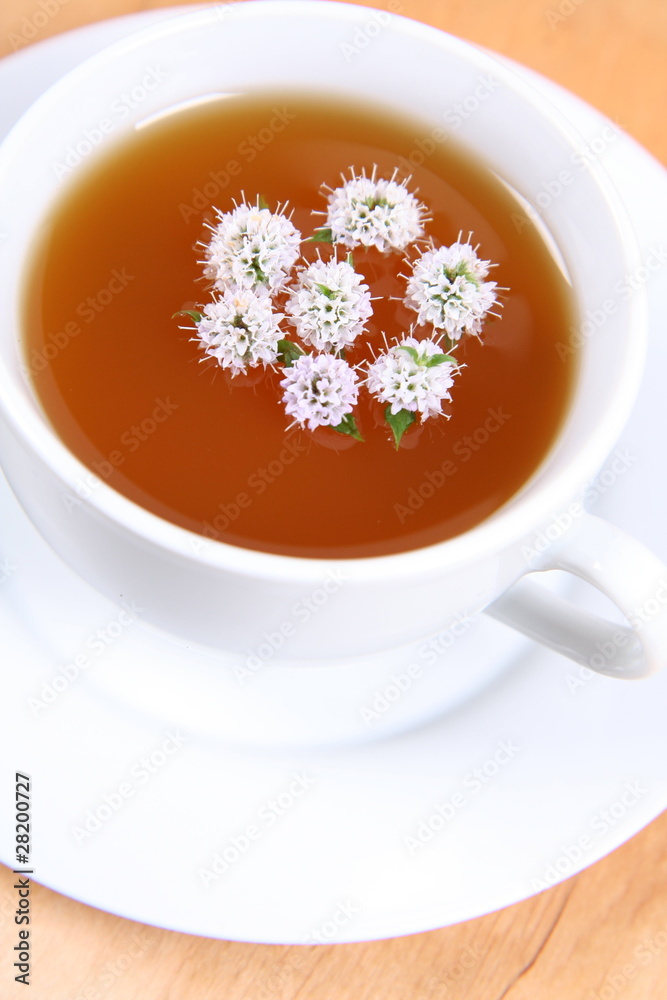 Cup of green tea with flowers of peppermint floating in it Cup of green tea with flowers of peppermint floating in it