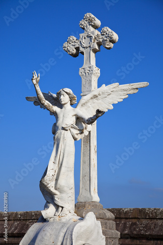 Angel statue and big stone cross on tombs in a cemetery