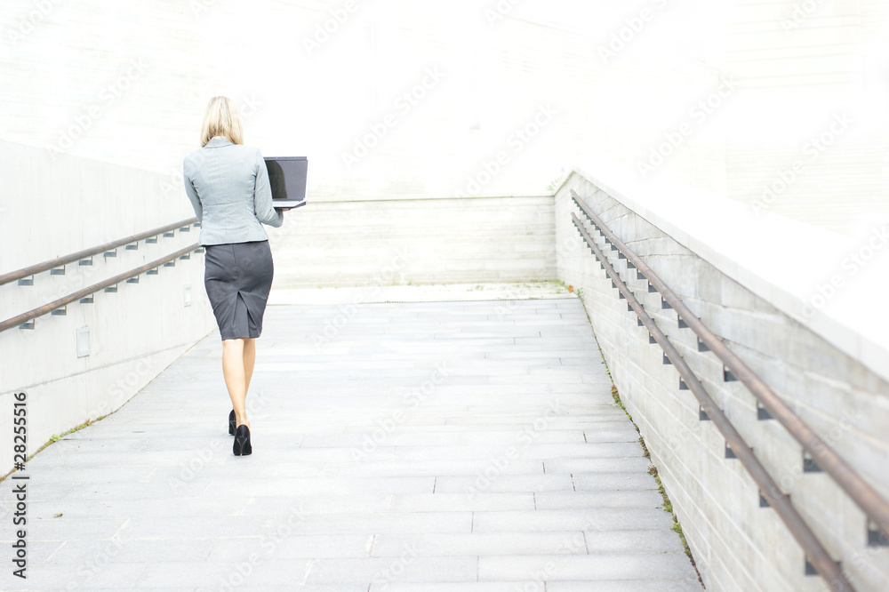 A young businesswoman is walking holding a laptop
