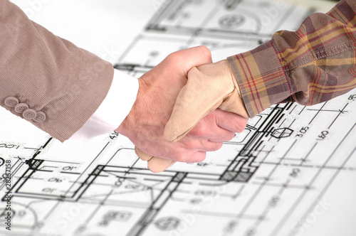 Worker and businessman shaking hands over house renovation plans