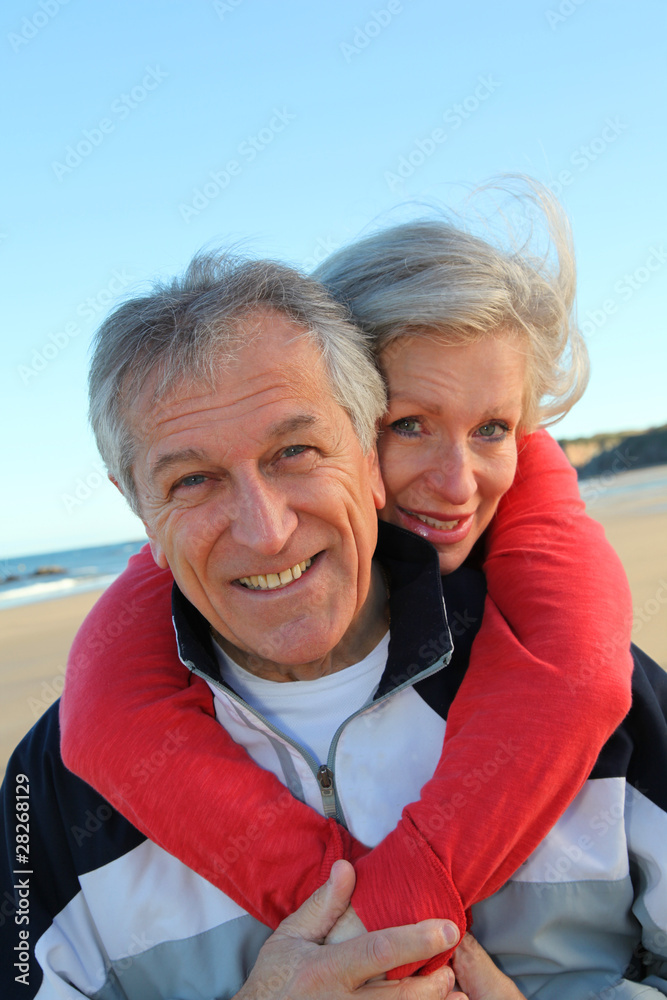 Senior man giving piggyback ride to woman by the sea