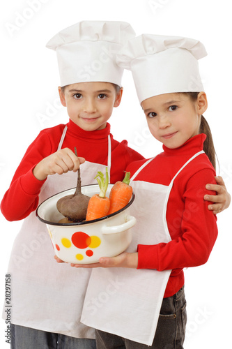 Two little chief-cookers holding a pot with vegetables