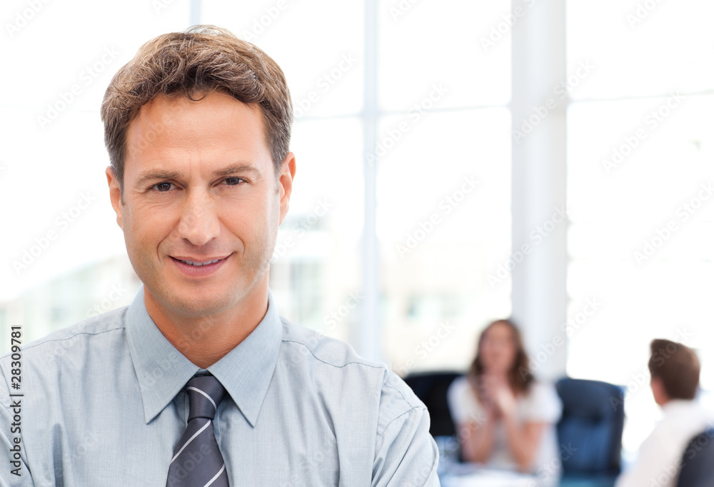Relaxed businessman posing in front of his team while working in Relaxed businessman posing in front of his team while working in