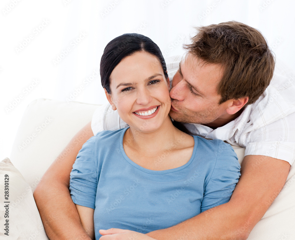 Lovely man kissing his girlfriend while relaxing on the sofa Lovely man kissing his girlfriend while relaxing on the sofa