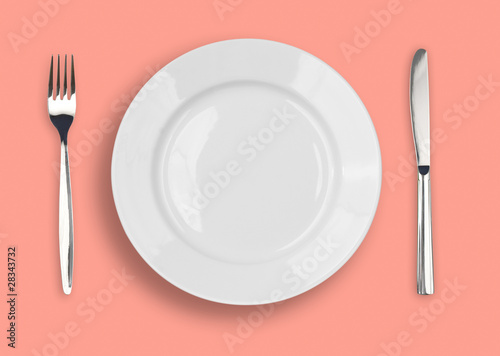 Knife, white plate and fork on rose background