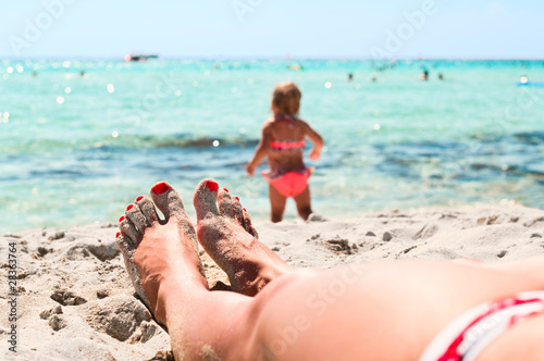 Legs of girl lying on sand and little playing child