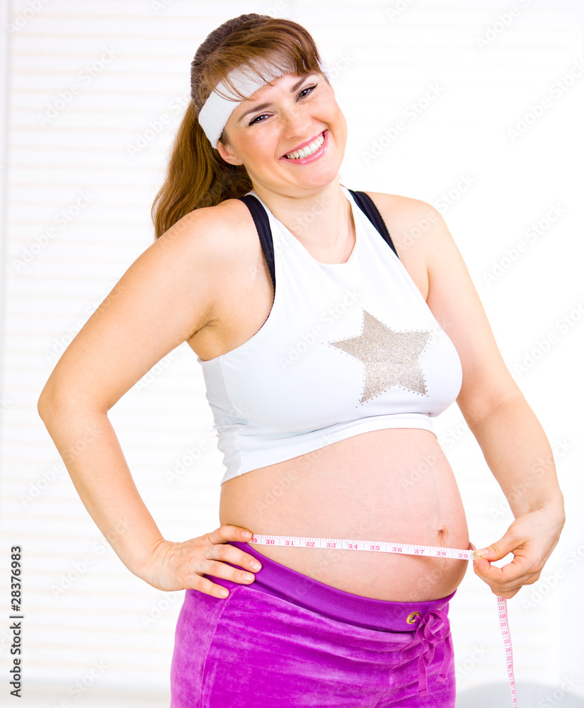 Laughing beautiful pregnant female measuring belly. Laughing beautiful pregnant female measuring belly.