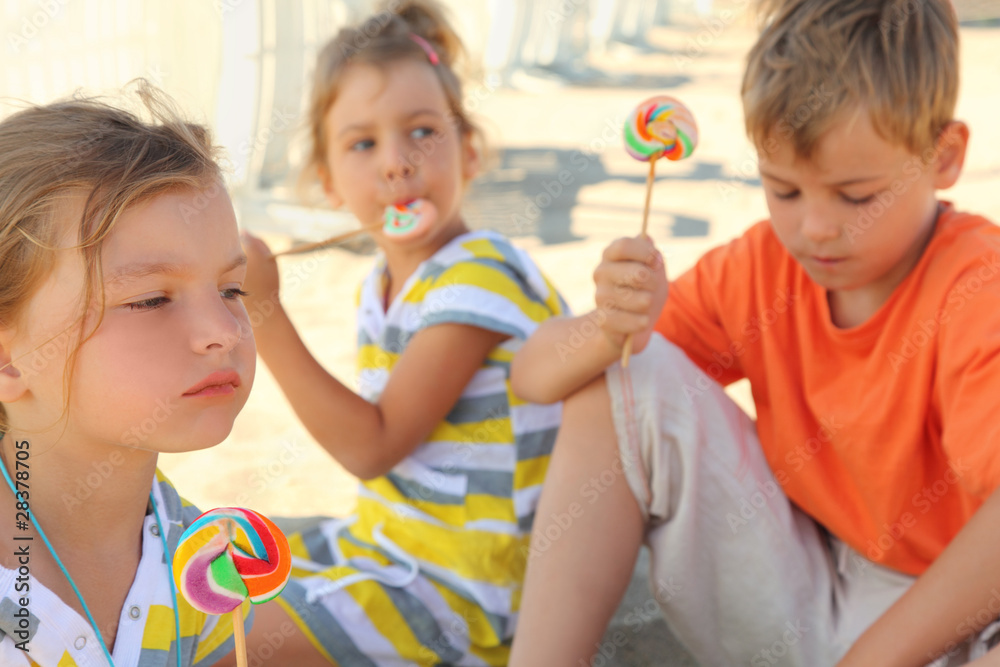serious children sitting on beach and eating lollipops serious children sitting on beach and eating lollipops
