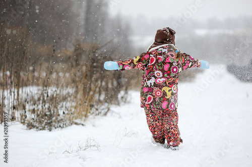 Small girl in colorful clothers plays with snow photo