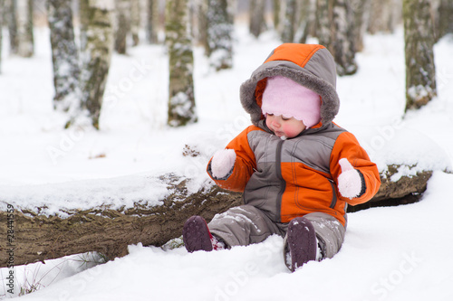 cute baby sit on snow in park and play with mittens