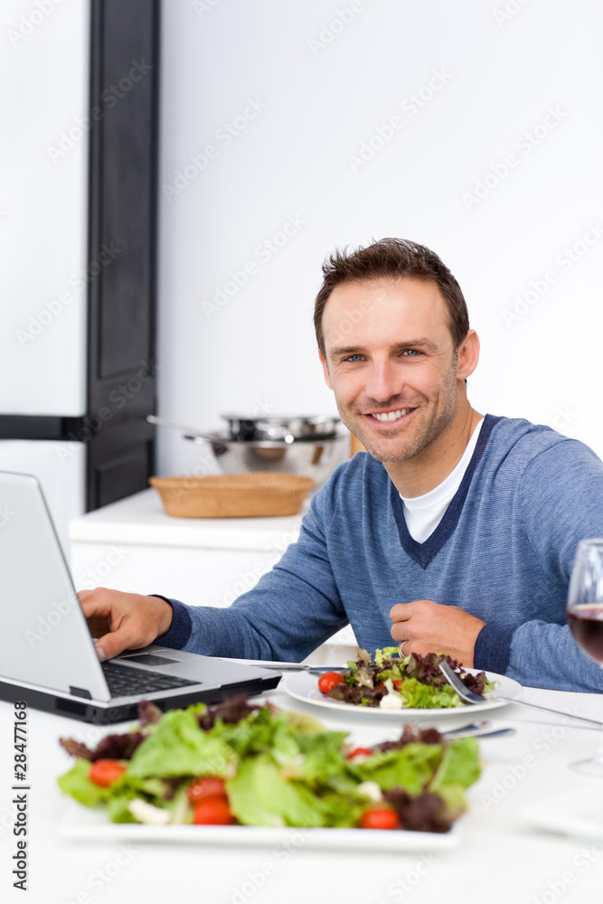 Cheerful man working on his laptop while having lunch Cheerful man working on his laptop while having lunch