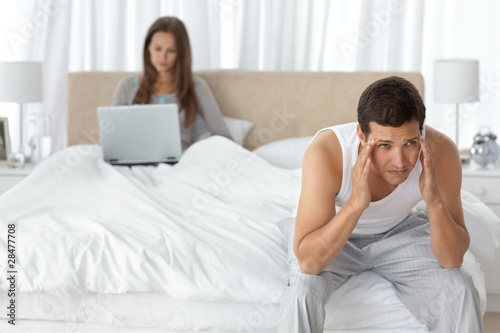 Man having a headache in the bedroom with his girlfriend