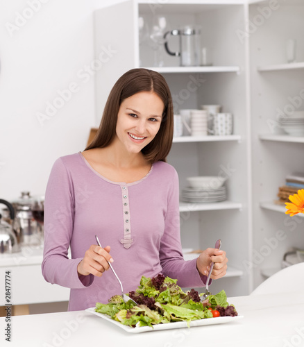 Pretty woman preparing a salad standing in the kitchen