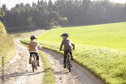 Two young children ride bicycles in park