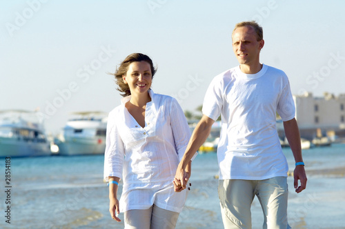 View of happy young couple walking on the beach, holding hands.