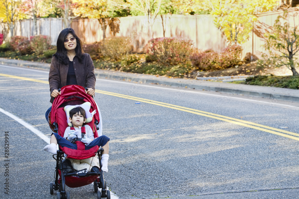 Mother walking with her disabled son in stroller outdoors Mother walking with her disabled son in stroller outdoors