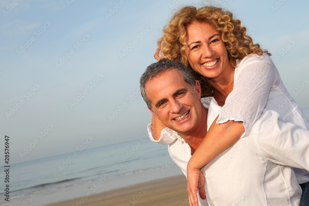 Portrait of happy mature couple at the beach - obrazy, fototapety, plakaty 