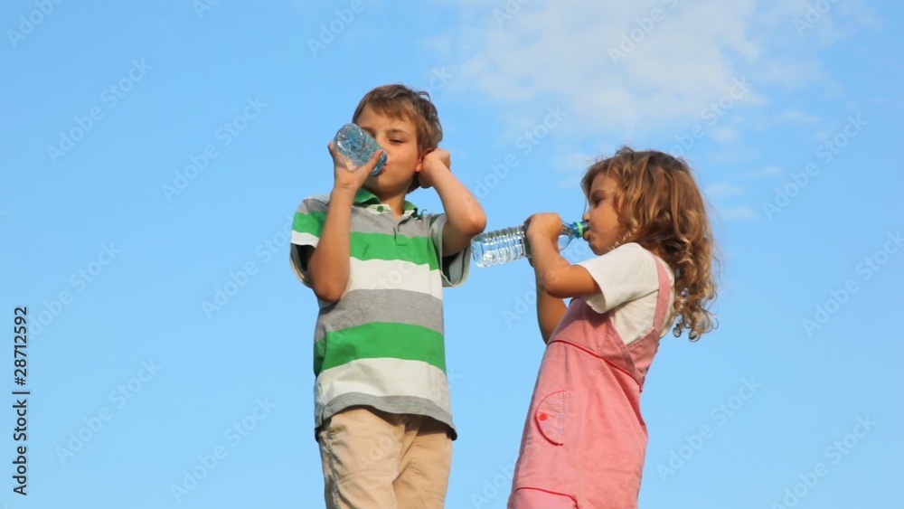 boy with girl standing and drink water from plastic bottles boy with girl standing and drink water from plastic bottles