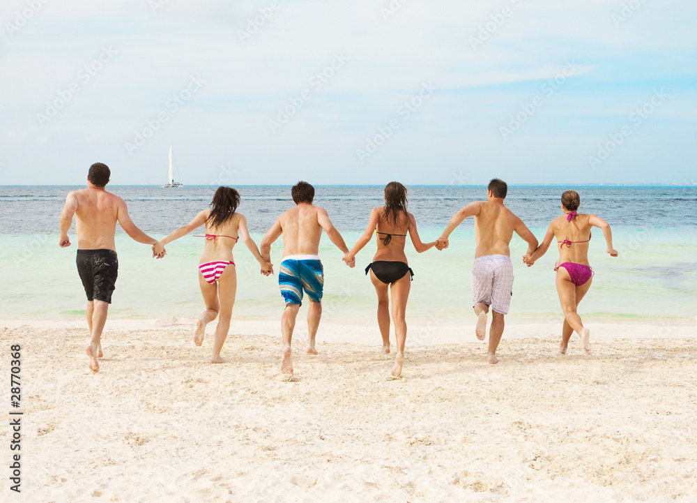 Group of young adults running together on the beach