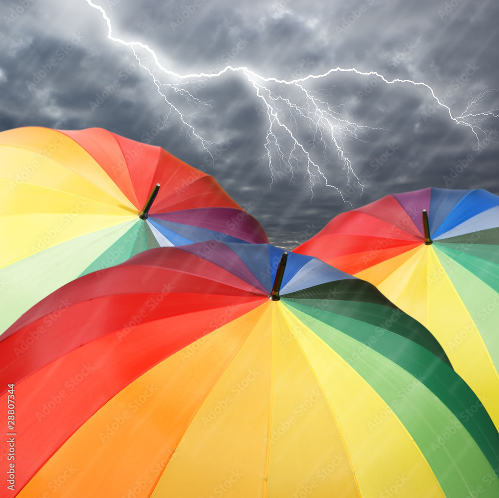 Rainbow umbrellas on dramatic sky background under rain
