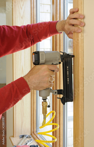 Nail gun being used to install wood trim around windows