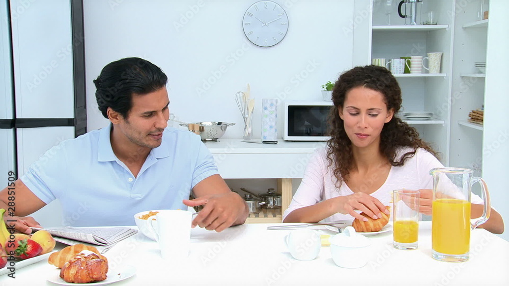 Man reading a newspaper during breakfast with his wife Man reading a newspaper during breakfast with his wife