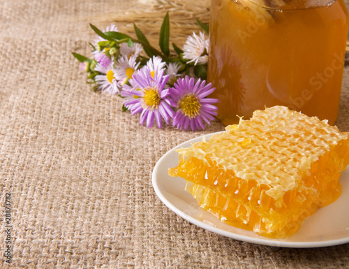 honeycomb, flowers and honey in pot on sack photo