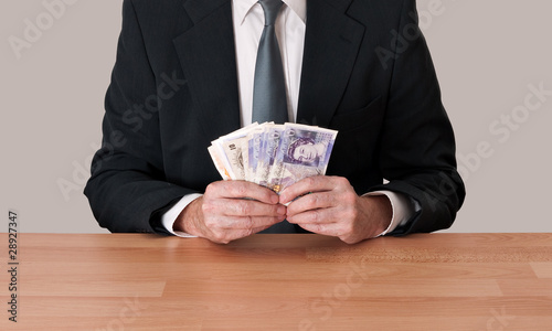 Man in suit sitting with cash - pounds sterling