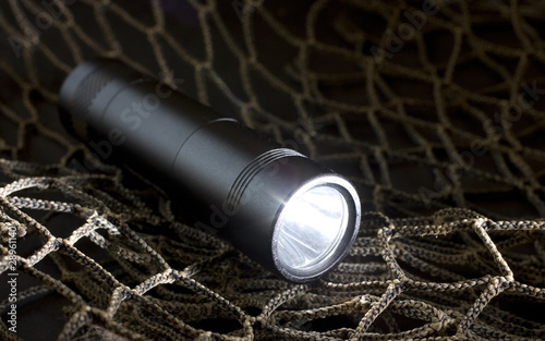 Aluminum tactical flashlight turned on resting on green netting photo