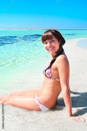 Young pretty girl sitting on sandy beach near shore blue sea
