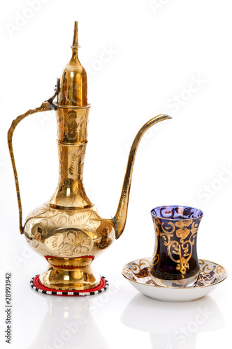 Arabic brass coffee pot with a welcoming a cup full of coffee.