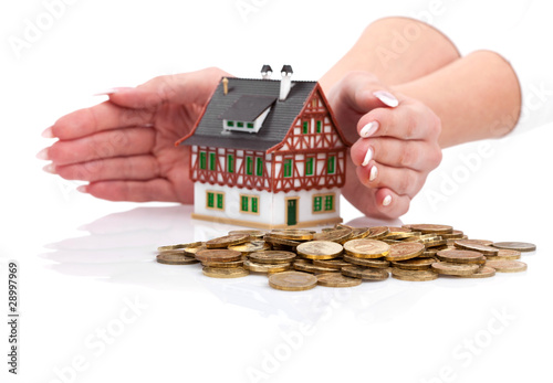 Womens hands protect miniature house with the coins. Focus on co