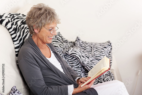 seniorin mit buch auf dem sofa photo