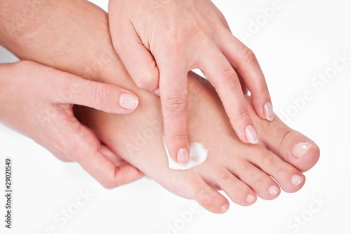 young woman applies cream on her foots. On a white background.